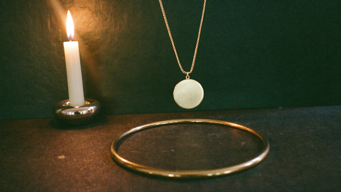 Goldener Armreif und feine Kette mit rundem Anhänger auf dunklem Stein, von einer Kerze warm beleuchtet
