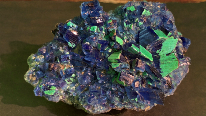 Nahaufnahme einer Azurit-Stufe mit tiefblauen, glänzenden Kristallen und grünen Malachit-Flecken auf dunklem Schiefer