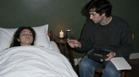 Channeling-Sitzung wie beim Ra-Material: eine Frau liegt mit geschlossenen Augen im Bett, ein Mann hält ihr ein Mikrofon hin und zeichnet mit einem Kassettenrekorder auf, daneben Kerze und Wasserkelch
