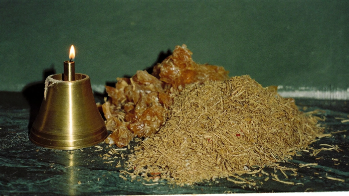 Goldene Weihrauch-Harztränen und Räucherwerk neben Messingleuchter bei Kerzenlicht vor dunkelgrüner Wand