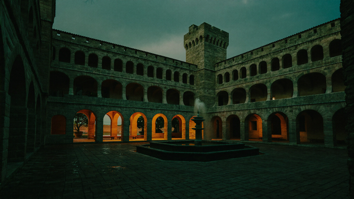Renaissance-Schlosshof mit drei Arkadengeschossen und einem Brunnen zur blauen Stunde, warmes Licht fällt von einer Seite durch die Bögen