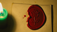 Rotes Wachssiegel mit Rosenprägung, am Rand aufgebrochen, auf hellem Papier neben einer brennenden Kerze