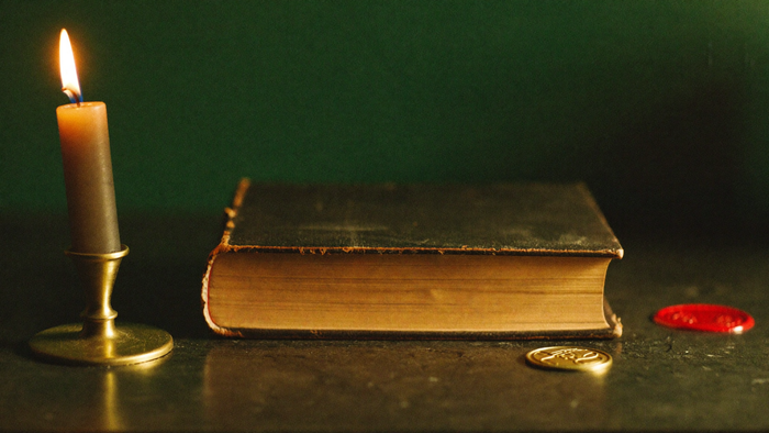 Geschlossenes altes Lederbuch mit Messingsiegel und rotem Wachssiegel bei Kerzenlicht vor dunkelgrüner Wand — Titelbild zum Lemegeton