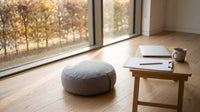Heller Raum mit Meditationskissen vor einem Fenster mit Herbstbäumen, daneben ein Tisch mit Laptop und Klemmbrett – KI-Illustration