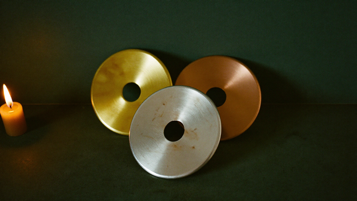 Drei Metallscheiben in Gold, Silber und Kupfer im Kerzenlicht vor grüner Wand