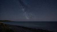 Klarer Sternenhimmel über einer dunklen Ostseeküste bei Nacht, ruhiges Wasser, kein Polarlicht