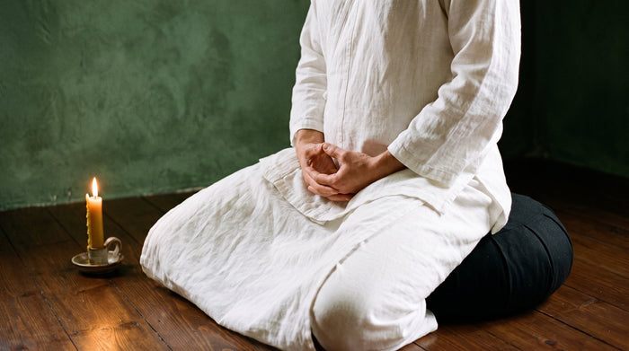 Person im Zen-Sitz auf schwarzem Kissen, die Hände ruhen vor dem Unterbauch, Kerzenlicht – Zen und Hara nach Dr. Rolf-Peter Adam