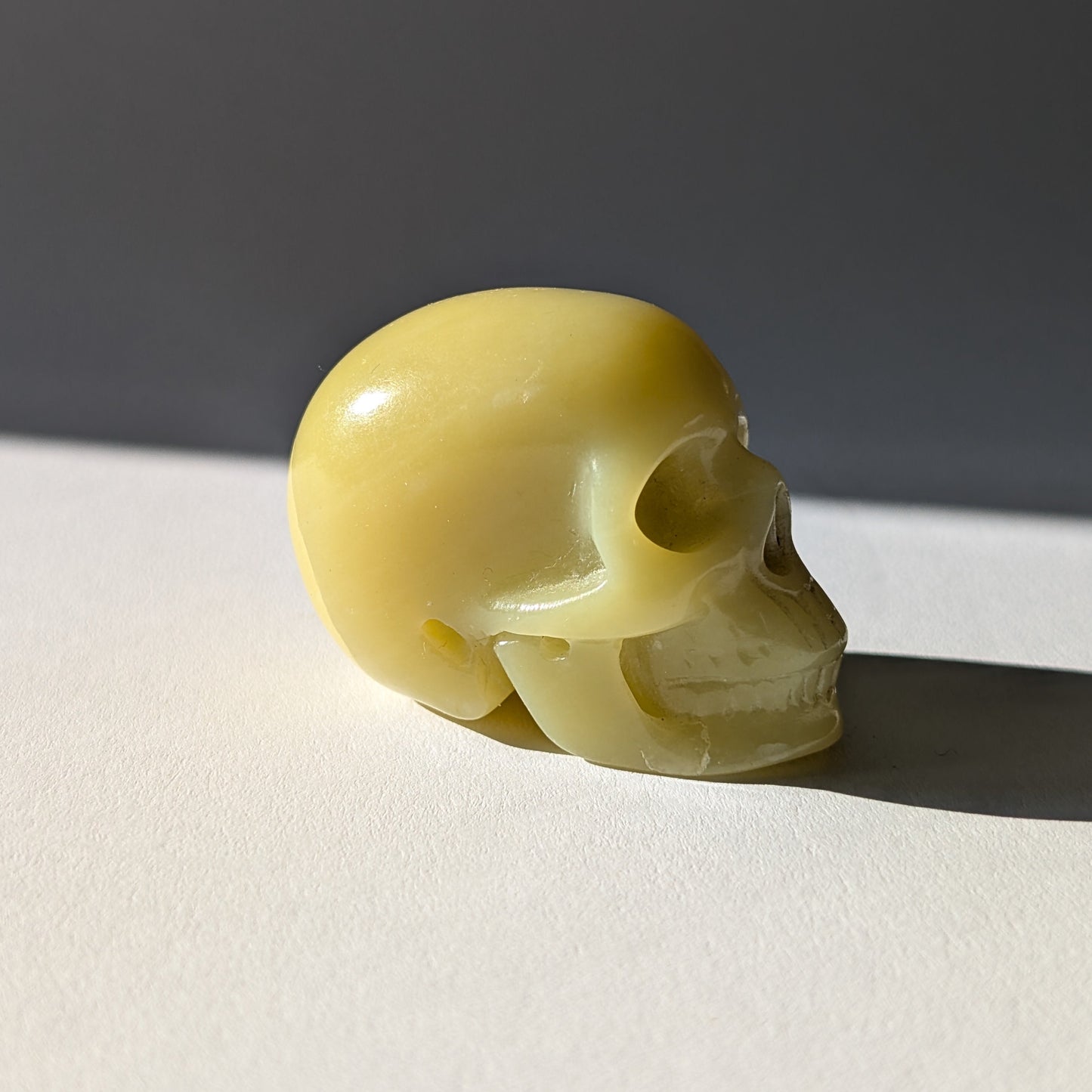 Kleiner Kristallschädel "Sentos" (78g) aus blassgrün-gelbem Jadeit im Licht.