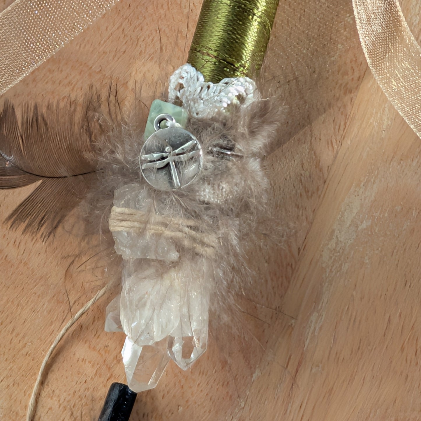 Handgefertigter Zauberstab mit einem goldgelben Citrin und schimmerndem Drusenquarz, verziert mit Federn und einem grünen Band, auf einer Holzplatte.