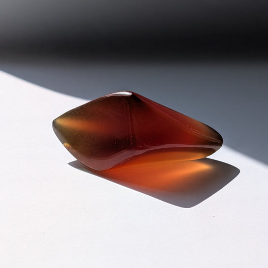 Bernstein Talisman "Funke der Vorzeit" in dunkler, tropfenartiger Form mit rotem Kern.