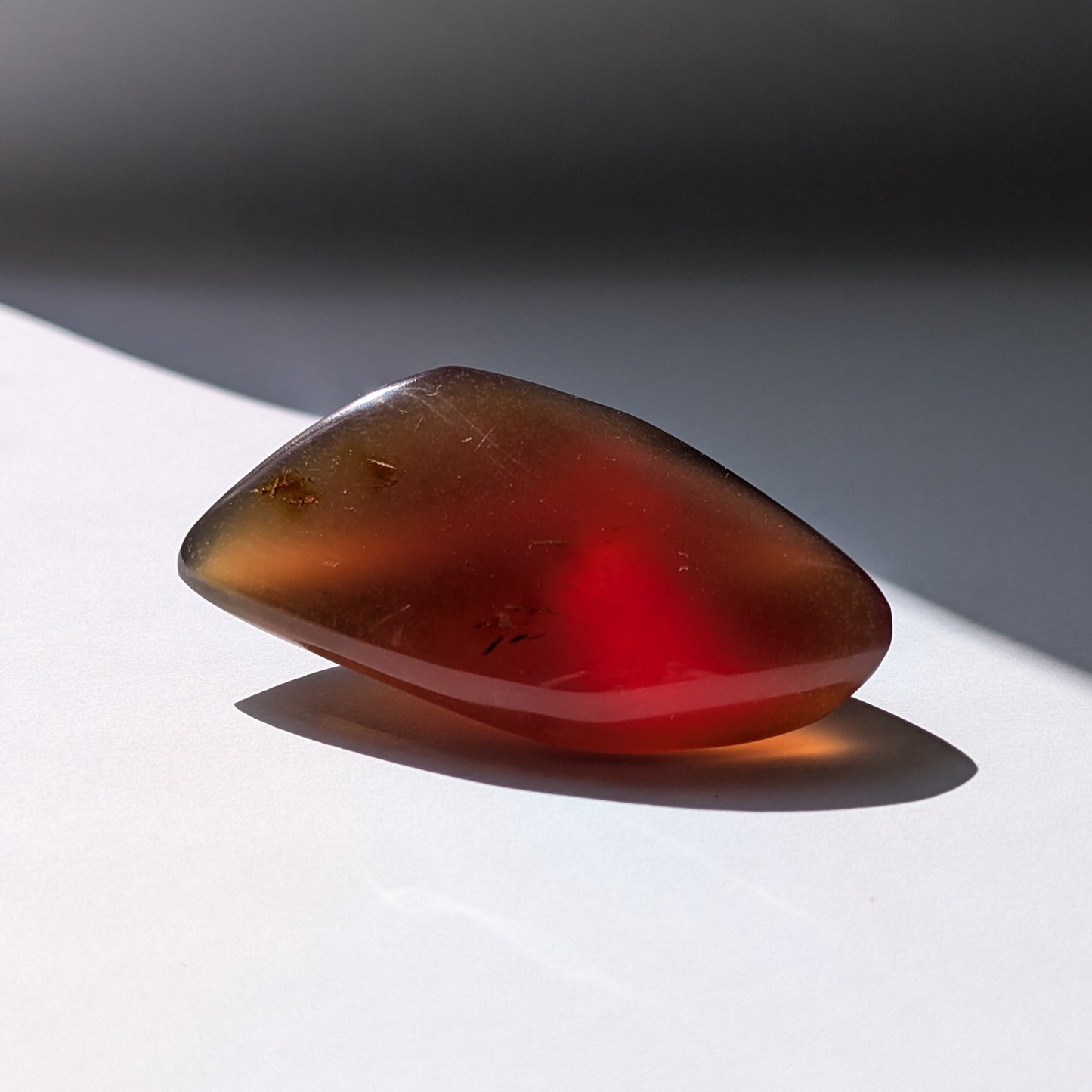 Bernstein Talisman "Funke der Vorzeit" in dunkler, tropfenartiger Form mit rotem Kern.