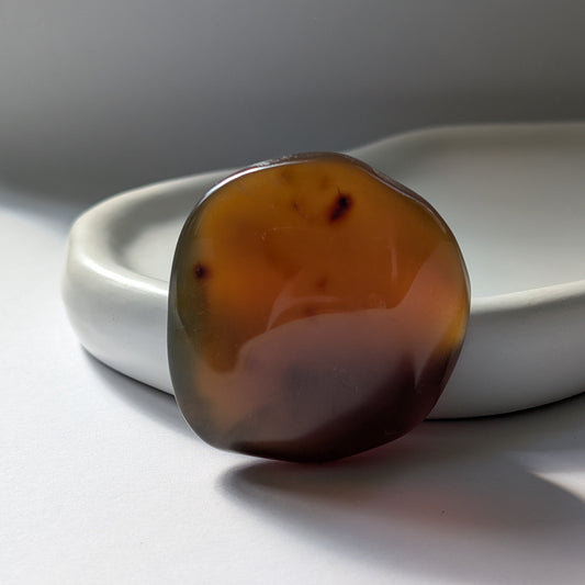 Bernstein Talisman "Tropfen der Vorzeit" in dunkler, tropfenartiger Form mit rotem Kern.