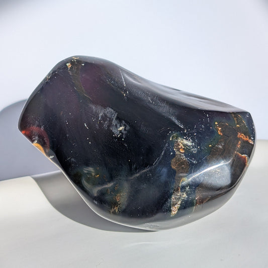 Bernstein Unikat "Der Monolith der Vorzeit" in dunkler, unregelmäßiger Form mit rotem Kern.