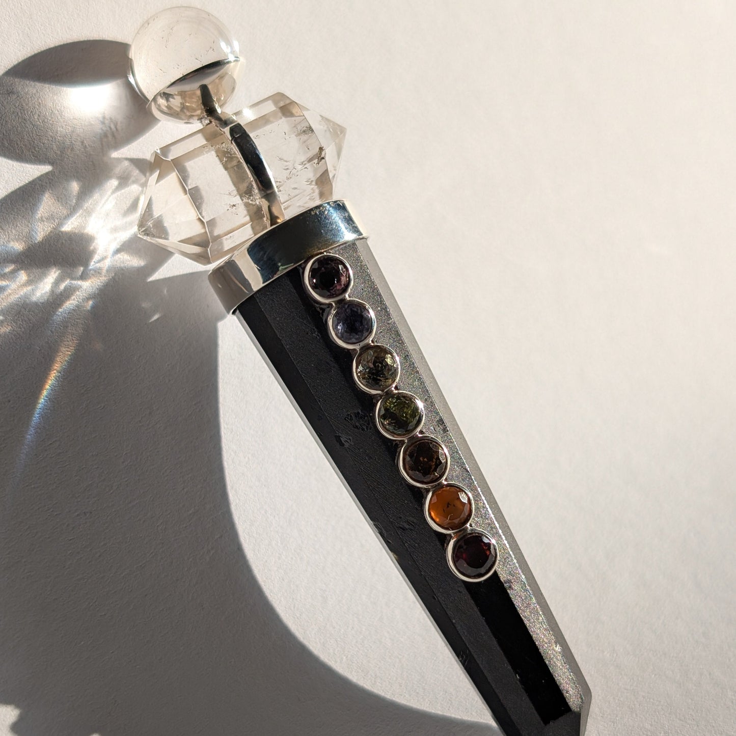 Chakra-Generatorstab aus schwarzem Schungit mit sieben farbigen Steinen und einer Bergkristall-Spitze.