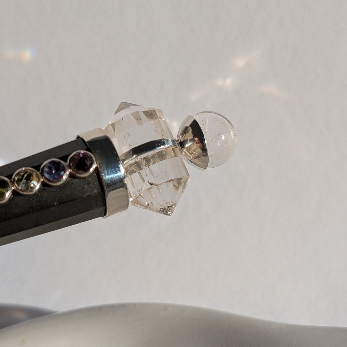 Chakra-Generatorstab aus schwarzem Schungit mit sieben farbigen Steinen und einer Bergkristall-Spitze.