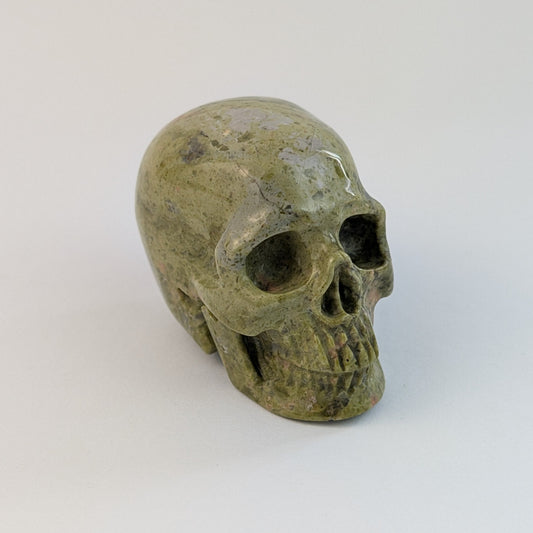 Ein 100g schwerer, handgeschnitzter Kristallschädel 'Haran' aus Unakit mit seiner charakteristischen Musterung aus moosgrünem Epidot und rosafarbenem Feldspat