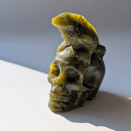 Ein 168g schwerer, handgeschnitzter Kristallschädel 'Veratha' aus grünem Serpentin, mit einer detailreichen Kobra, die sich auf seinem Scheitel aufrichtet.