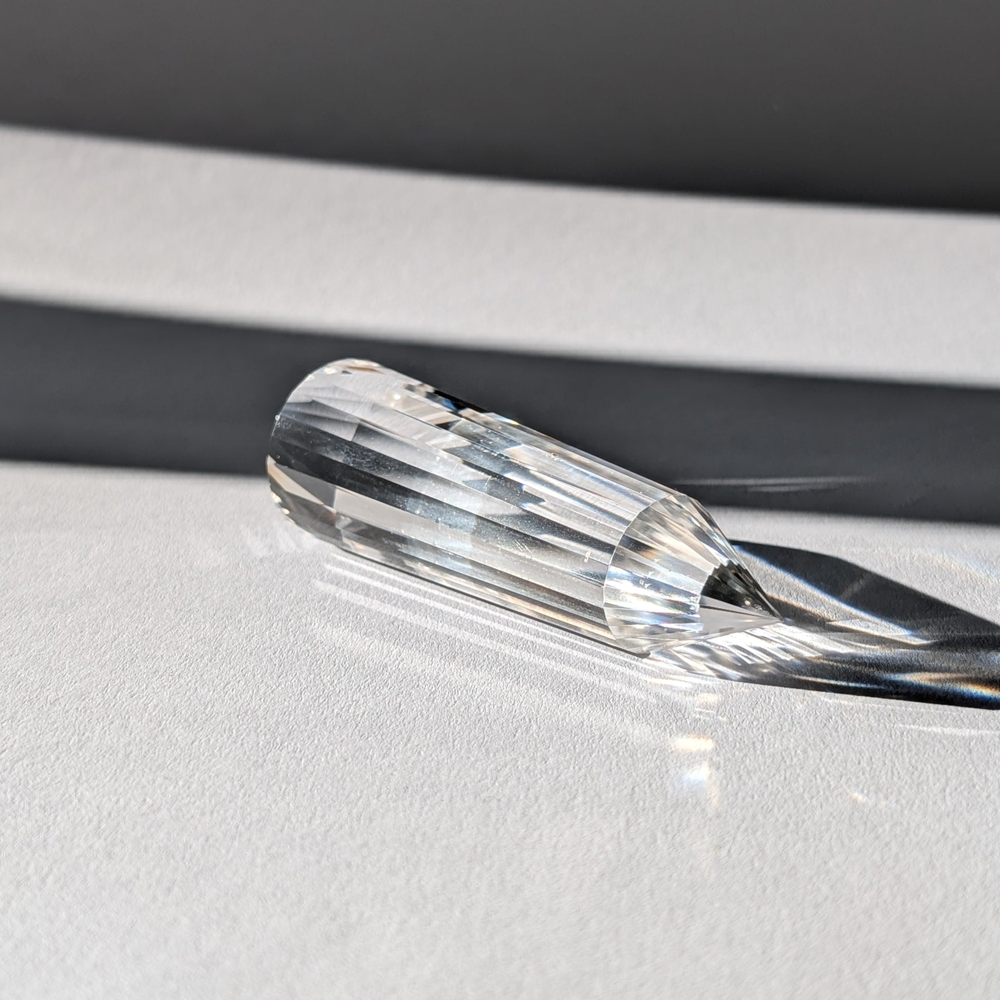 Ein 24-Facetten Vogel-Kristall aus wasserklarem Bergkristall, liegend im Sonnenlicht, das sich in ihm bricht.