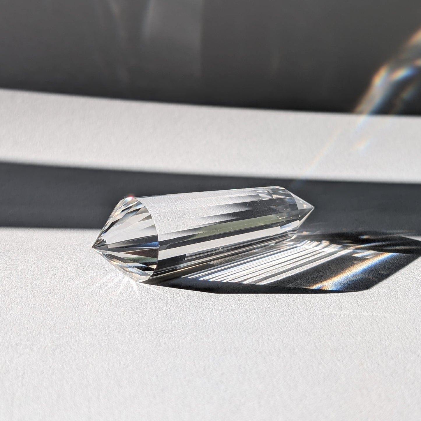 Ein 24-Facetten Vogel-Kristall aus wasserklarem Bergkristall, liegend im Sonnenlicht, das sich in ihm bricht.