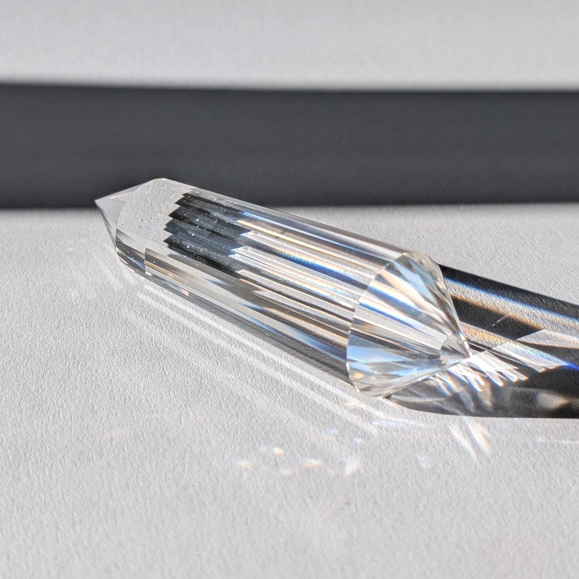 Ein 24-Facetten Vogel-Kristall aus wasserklarem Bergkristall, liegend im Sonnenlicht, das sich in ihm bricht.