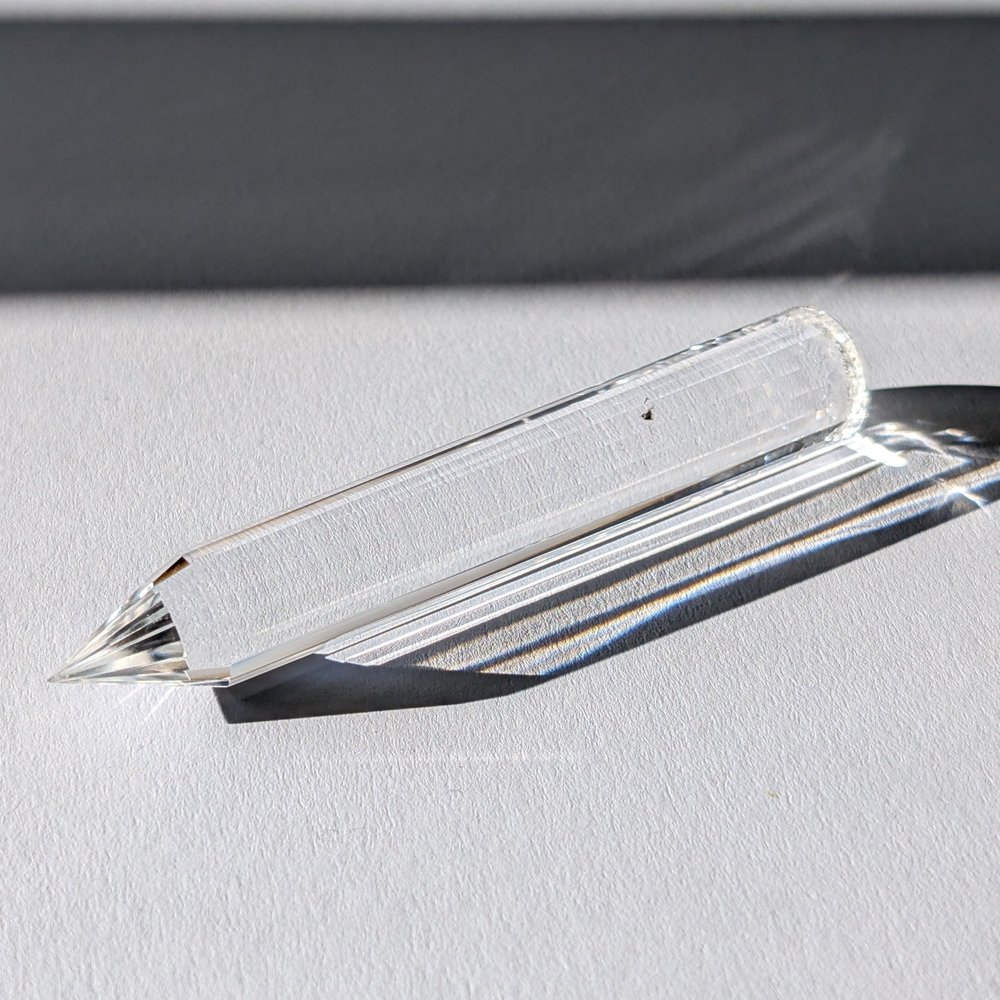 Ein 24-fach gerillter (fluted) Heilerstab aus wasserklarem Bergkristall (50g), der Licht reflektiert.