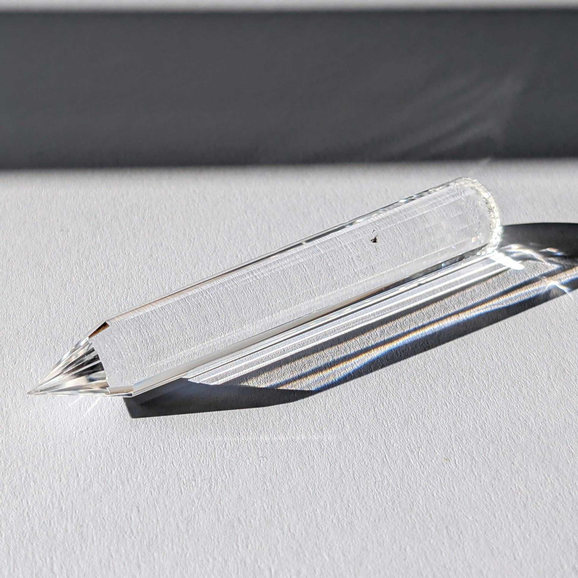 Ein 24-fach gerillter (fluted) Heilerstab aus wasserklarem Bergkristall (50g), der Licht reflektiert.