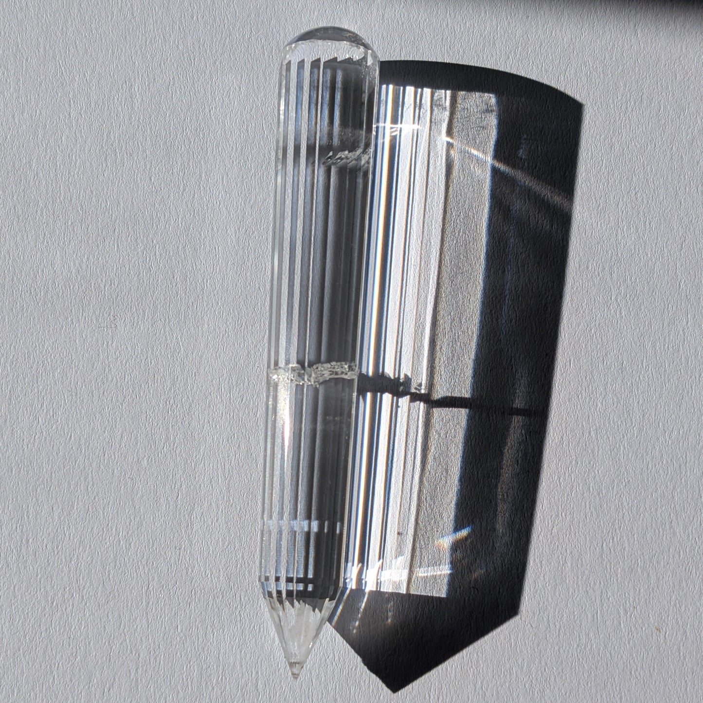 Ein 24-fach gerillter (fluted) Heilerstab aus wasserklarem Bergkristall (59g) im Licht.