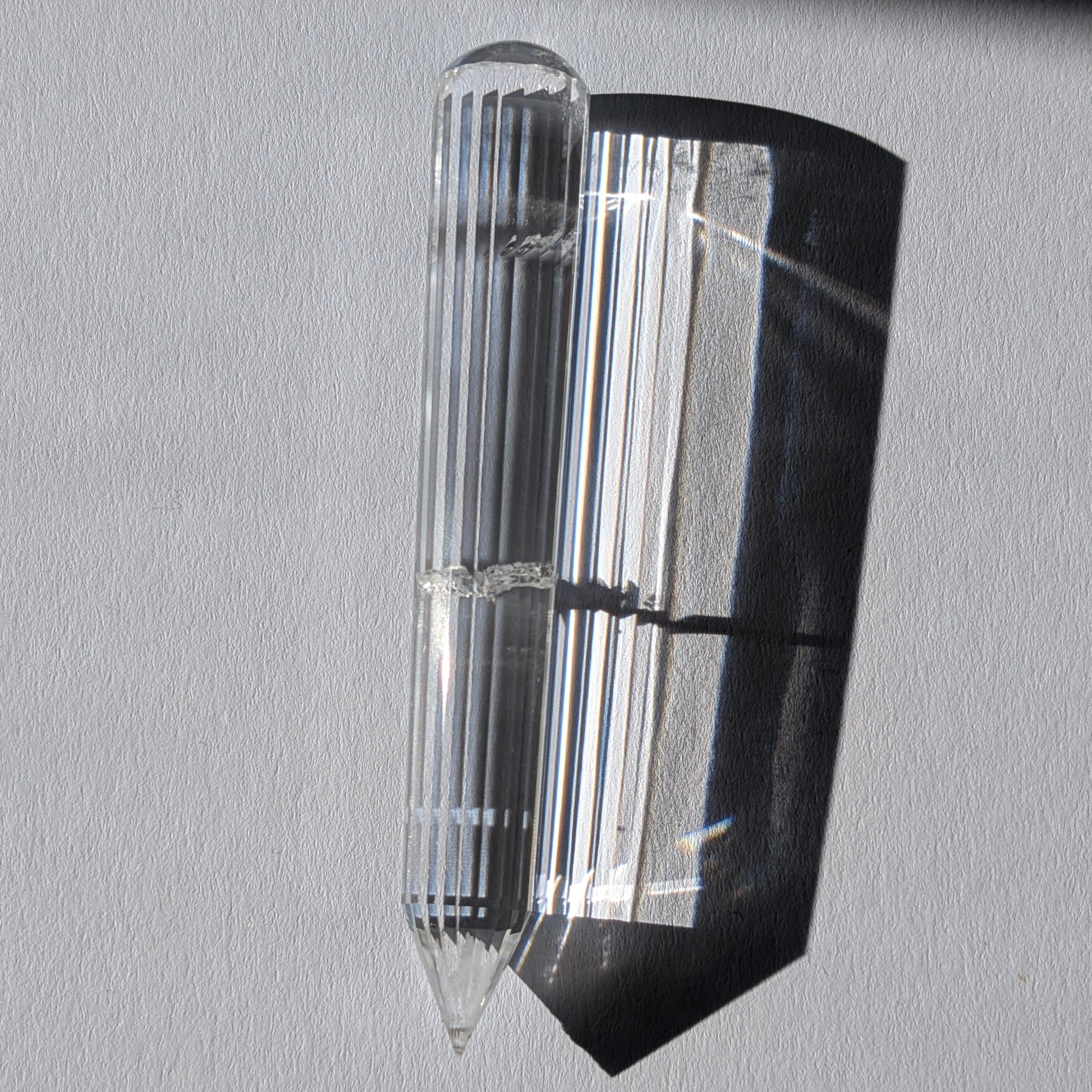 Ein 24-fach gerillter (fluted) Heilerstab aus wasserklarem Bergkristall (59g) im Licht.