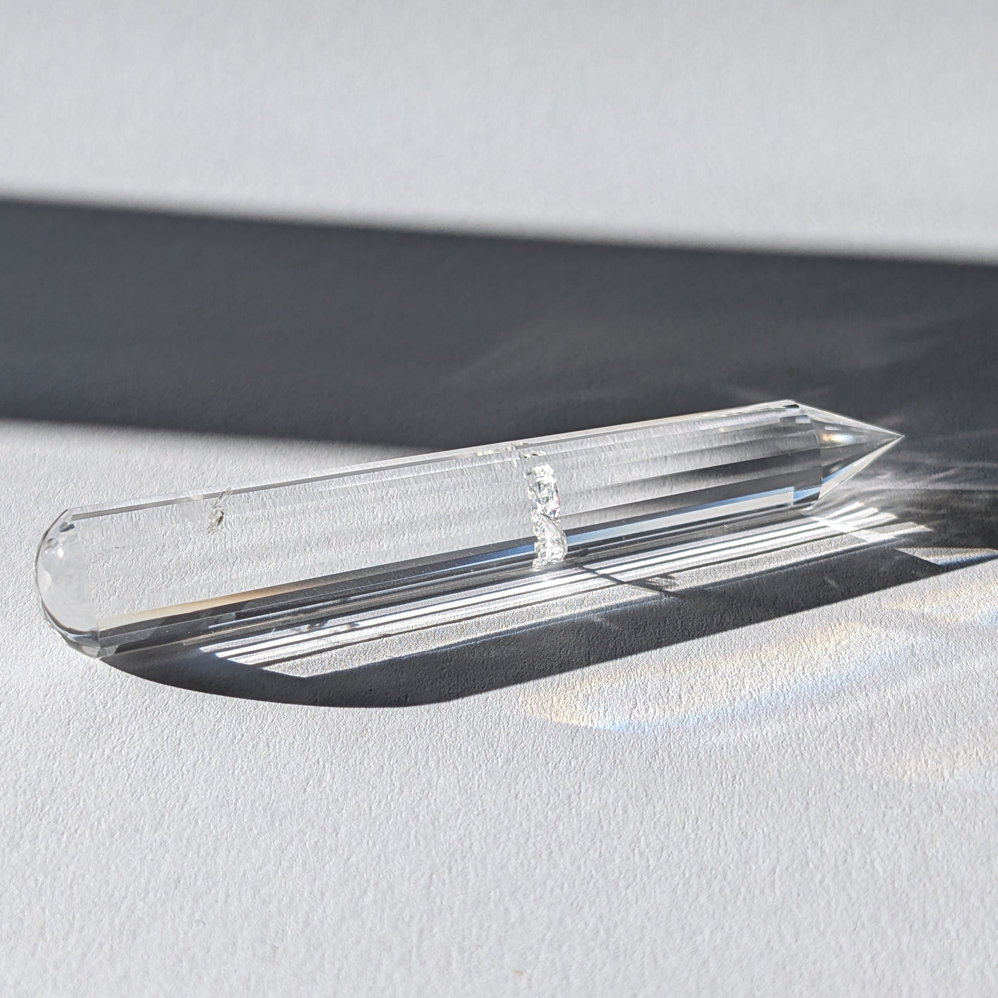 Ein 24-fach gerillter (fluted) Heilerstab aus wasserklarem Bergkristall (59g) im Licht.