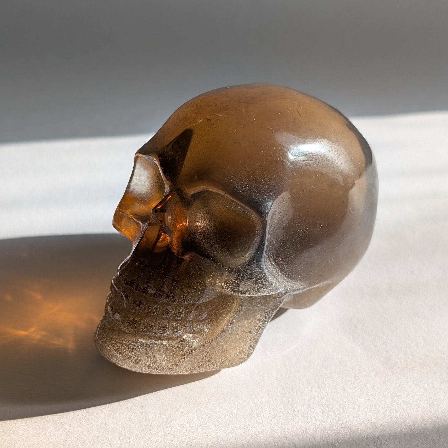 Ein 258g schwerer, synthetischer Rauchquarz-Schädel 'Auric' mit unzähligen goldenen Partikeln, die wie Sternenstaub im Licht funkeln.