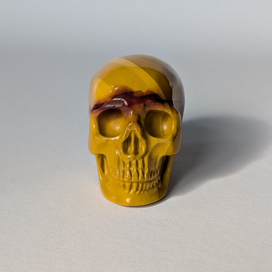 Ein 84g schwerer, handgeschnitzter Kristallschädel 'Ortah' aus Mookait mit einer einzigartigen Maserung in erdigen Gelb- und Rottönen.