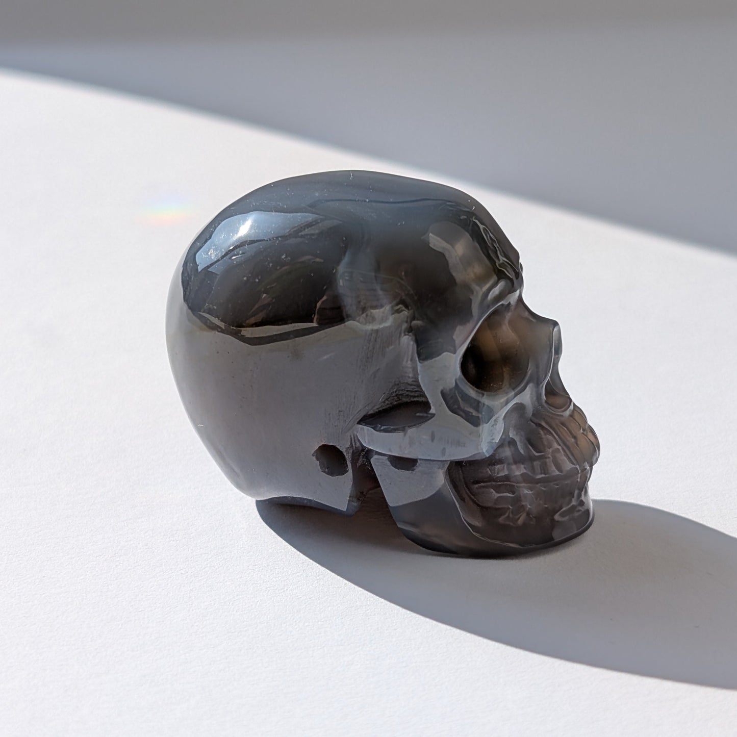 Ein 86g schwerer Kristallschädel 'Der Wächter der zwei Welten' aus Gebändertem Achat, dessen eine Hälfte eine offene, funkelnde Druzy-Geode ist.