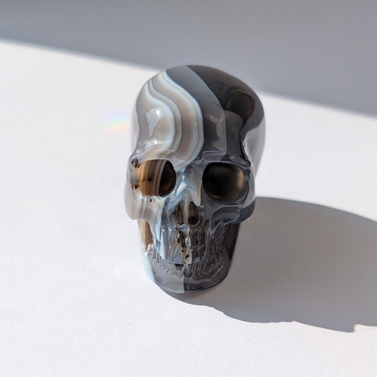 Ein 86g schwerer Kristallschädel 'Der Weber des Gleichgewichts' aus Gebändertem Achat mit hypnotischen, kontrastreichen Bändern in Schwarz, Grau und Weiß.