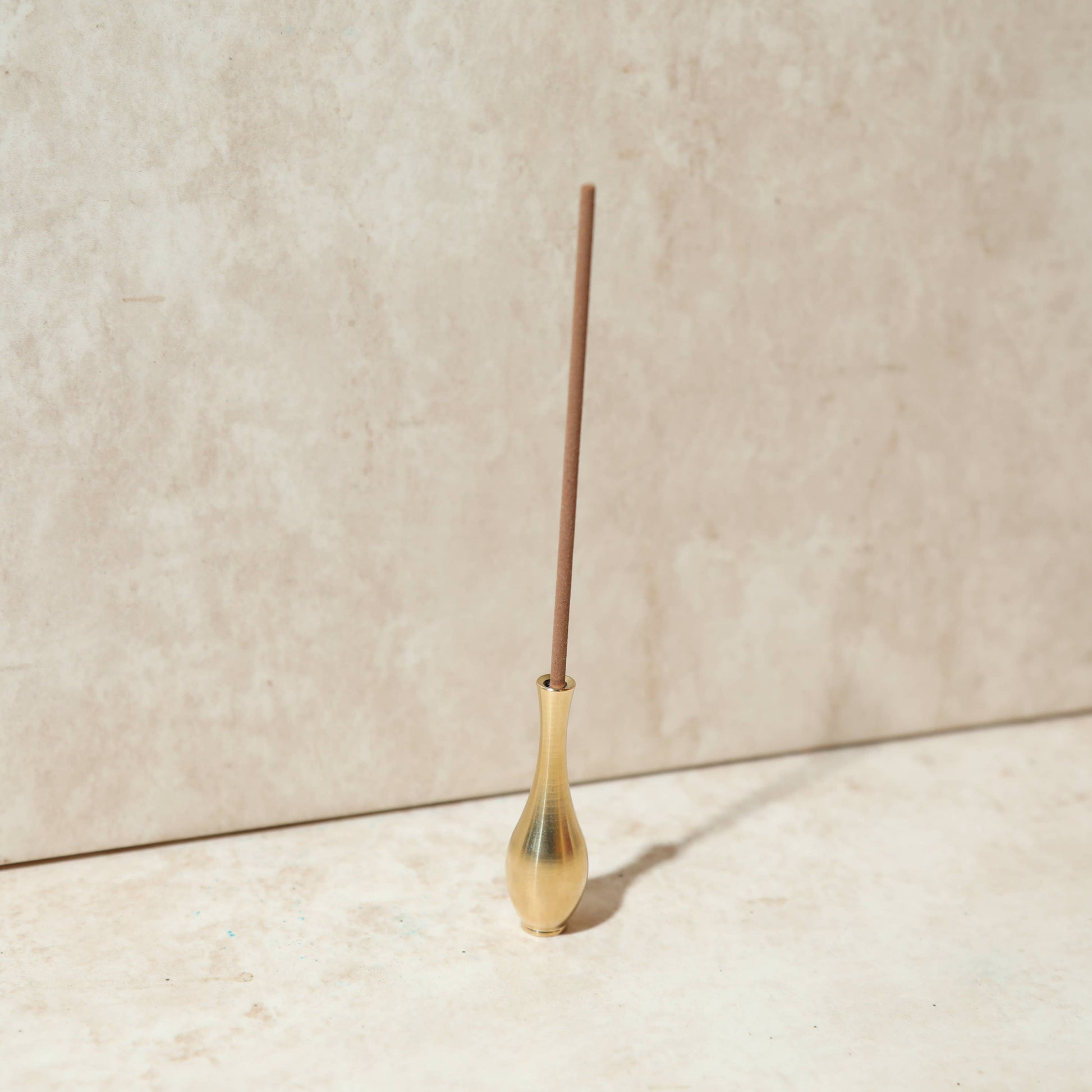 Ein eleganter, vasenförmiger Räucherstäbchenhalter 'Altar-Vase' aus massivem Messing, der ein Räucherstäbchen hält.