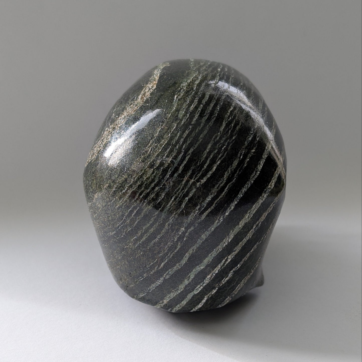Ein monumentaler, 1204g schwerer Kristallschädel 'Scryer' aus dunkelgrünem Serpentin mit hypnotisierendem, silbrigem Schimmer.
