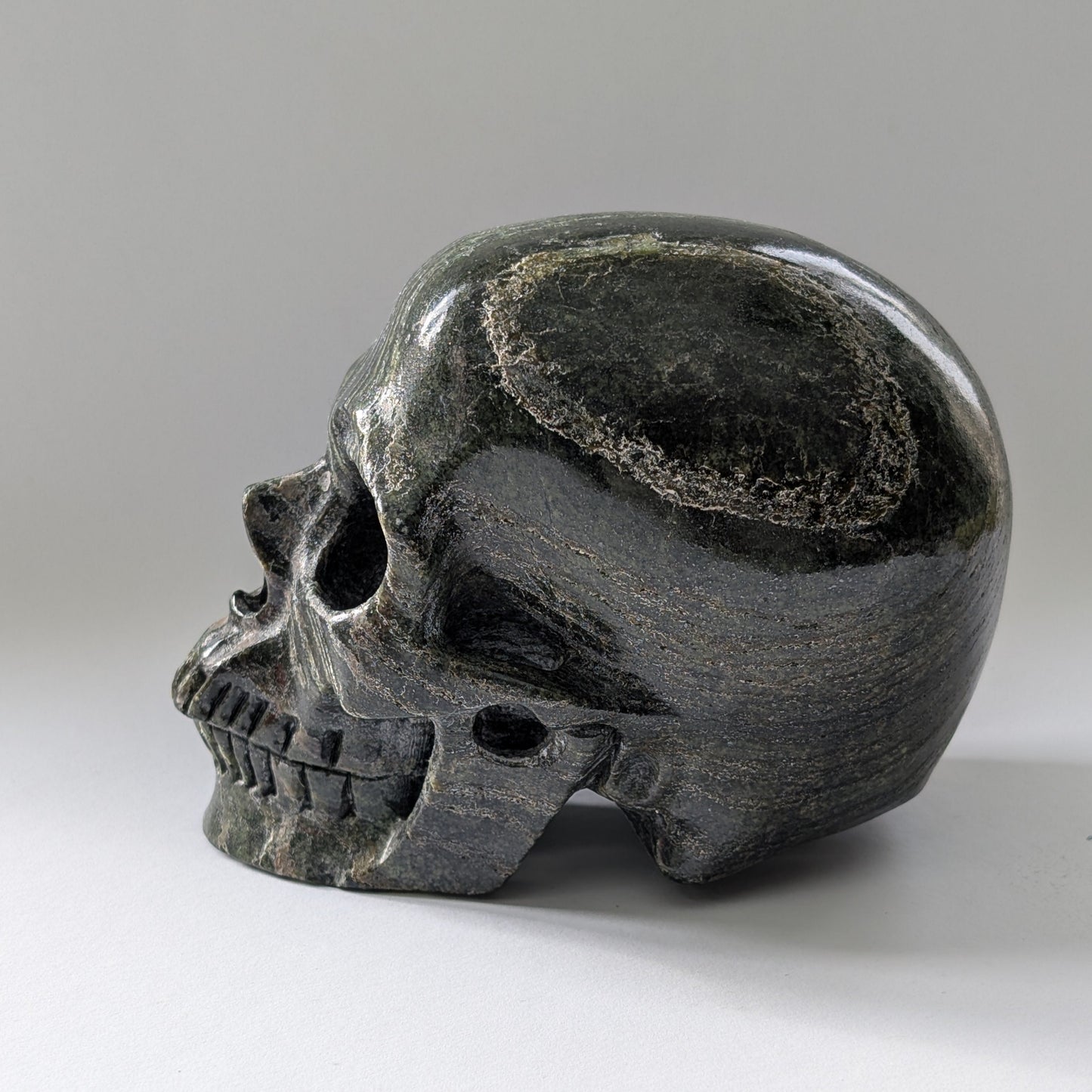 Ein monumentaler, 1204g schwerer Kristallschädel 'Scryer' aus dunkelgrünem Serpentin mit hypnotisierendem, silbrigem Schimmer.