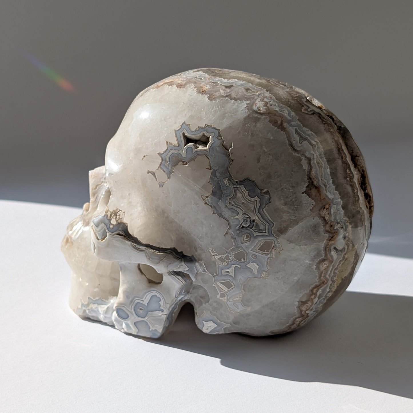 Ein monumentaler, 1292g schwerer Kristallschädel 'Der Wächter der Freude' aus Crazy Lace Achat mit hypnotischen Mustern und einer großen, offenen Druzy-Geode am Hinterkopf.