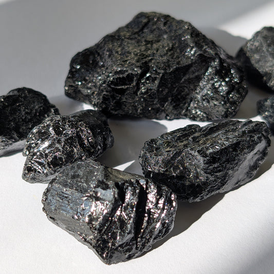Eine Gruppe von rohen, tiefschwarzen Turmalin-Brocken (Schörl) mit glasartigem Glanz auf einer weißen Oberfläche.