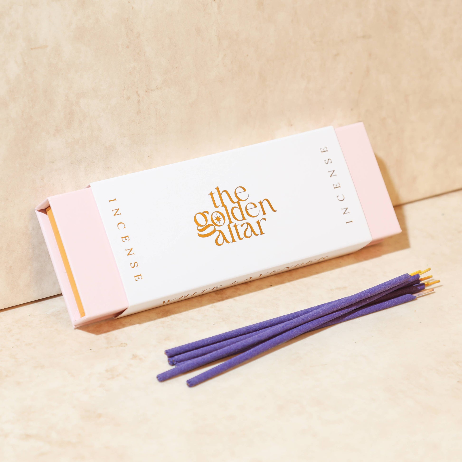 Eine cremeweiße Box von The Golden Altar mit 30 lila Weiße Lavendel Räucherstäbchen, die daneben liegen.