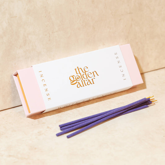 Eine cremeweiße Box von The Golden Altar mit 30 lila Weiße Lavendel Räucherstäbchen, die daneben liegen.