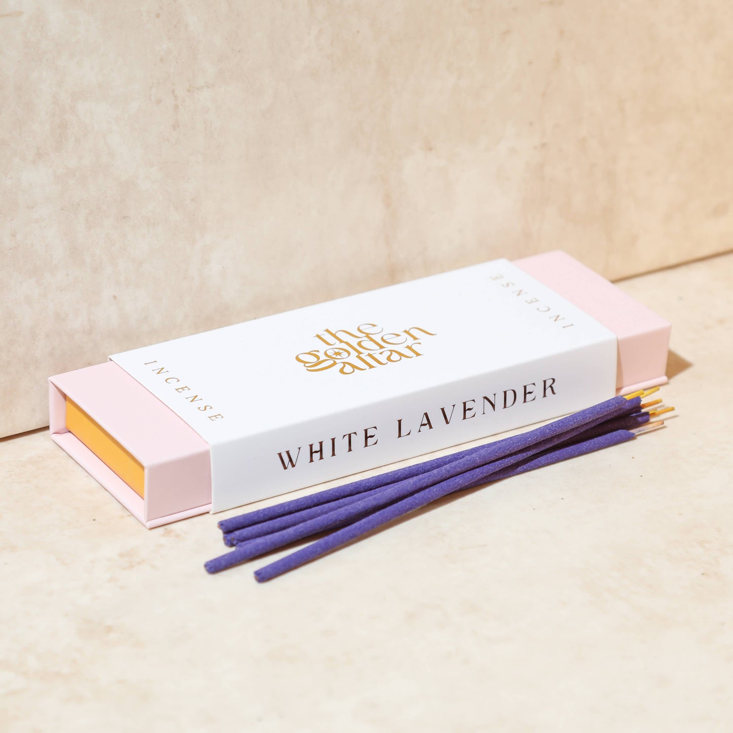 Eine cremeweiße Box von The Golden Altar mit 30 lila Weiße Lavendel Räucherstäbchen, die daneben liegen.