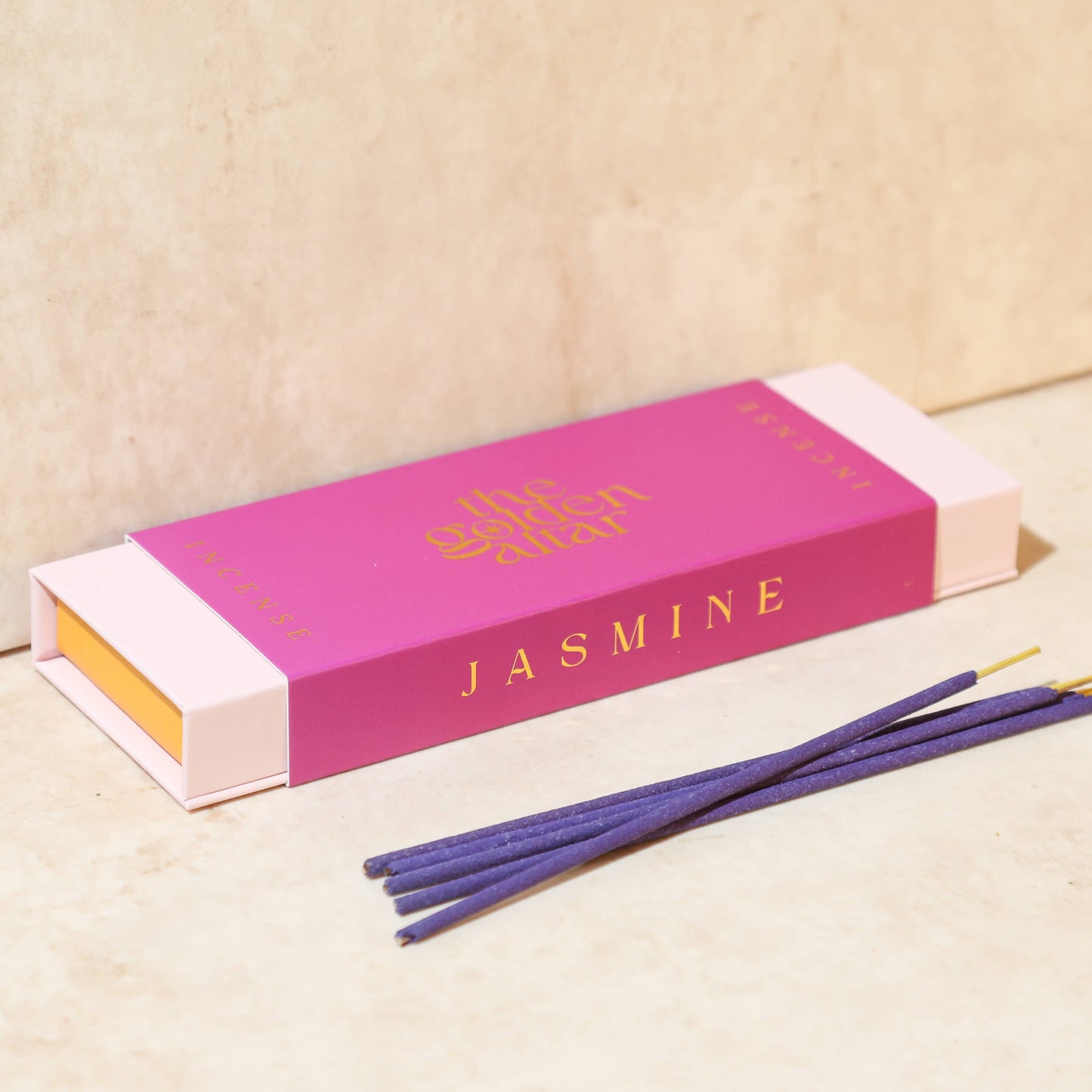 Eine fuchsiafarbene Box von The Golden Altar mit 30 dunklen Jasmin Räucherstäbchen, die daneben liegen.