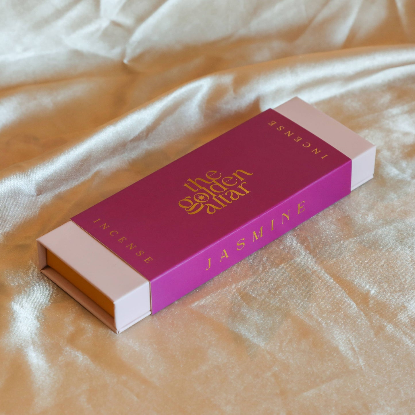 Eine fuchsiafarbene Box von The Golden Altar mit 30 dunklen Jasmin Räucherstäbchen, die daneben liegen.