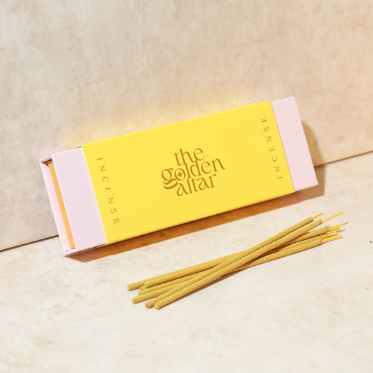 Eine goldgelbe Box von The Golden Altar mit 30 Ylang Ylang Räucherstäbchen, die daneben liegen.