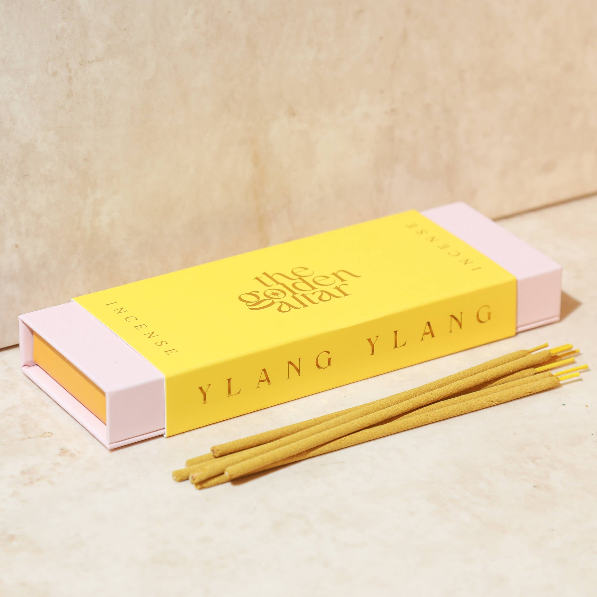 Eine goldgelbe Box von The Golden Altar mit 30 Ylang Ylang Räucherstäbchen, die daneben liegen.