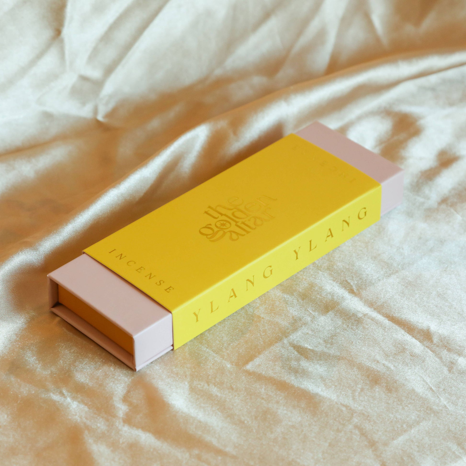Eine goldgelbe Box von The Golden Altar mit 30 Ylang Ylang Räucherstäbchen, die daneben liegen.