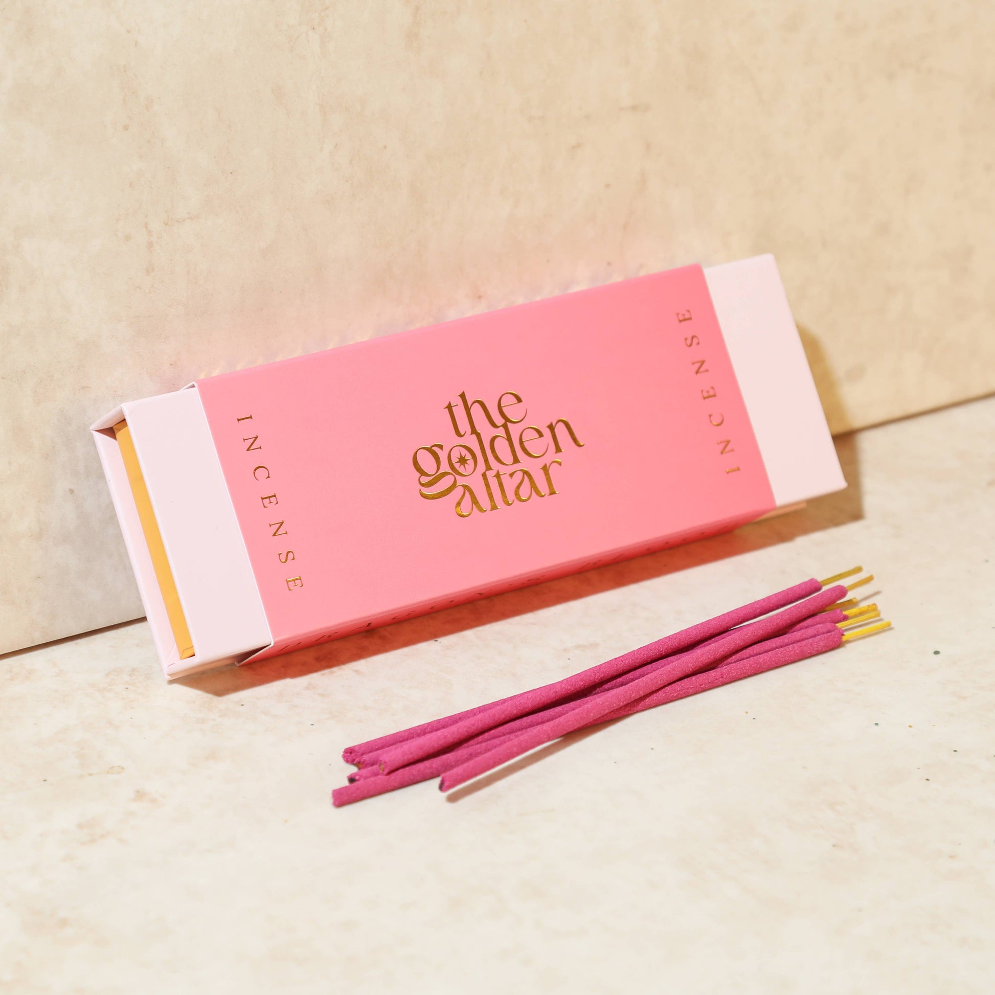 Eine leuchtend pinke Box von The Golden Altar mit 30 roten Drachenblut Räucherstäbchen, die daneben liegen.