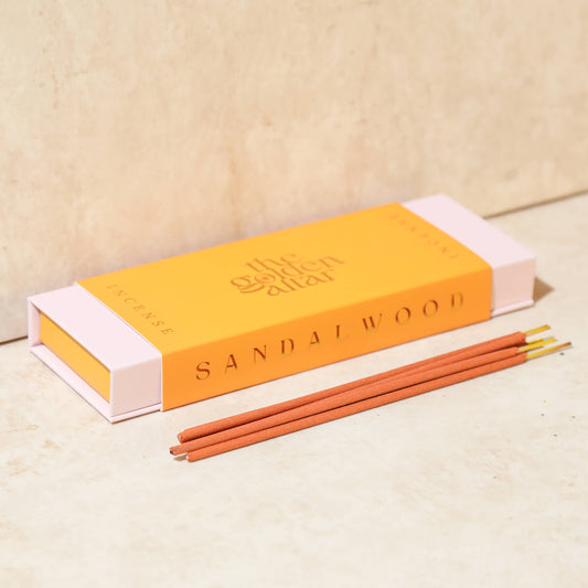 Eine orangefarbene Box von The Golden Altar mit 30 Sandelholz Räucherstäbchen, die daneben liegen.