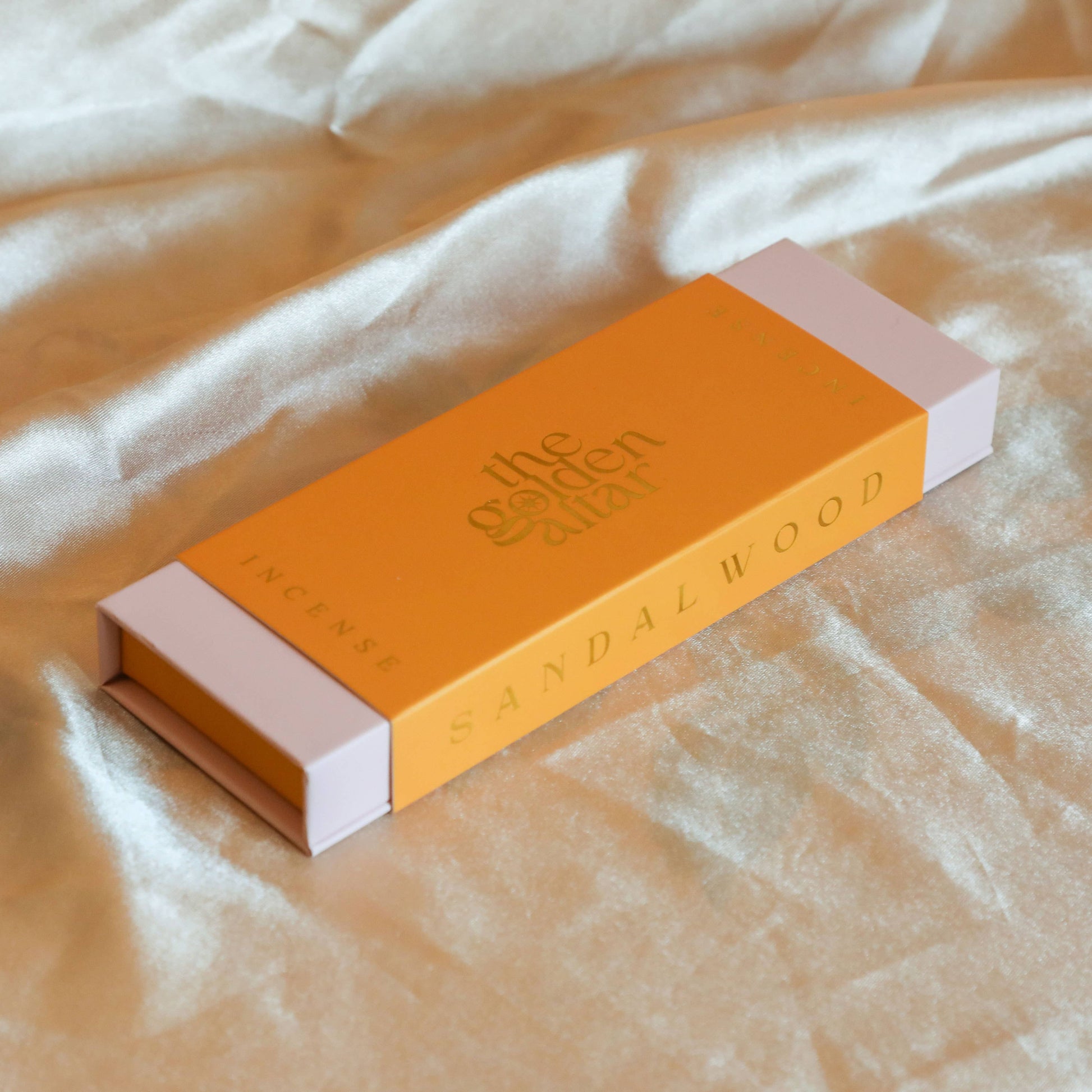 Eine orangefarbene Box von The Golden Altar mit 30 Sandelholz Räucherstäbchen, die daneben liegen.