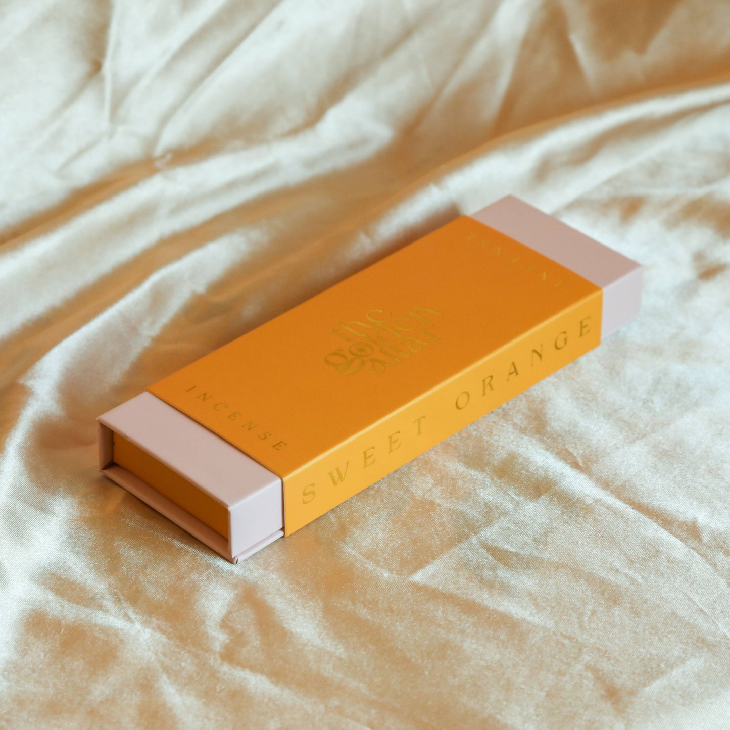Eine orangefarbene Box von The Golden Altar mit 30 orangefarbenen Süße Orange Räucherstäbchen, die daneben liegen.